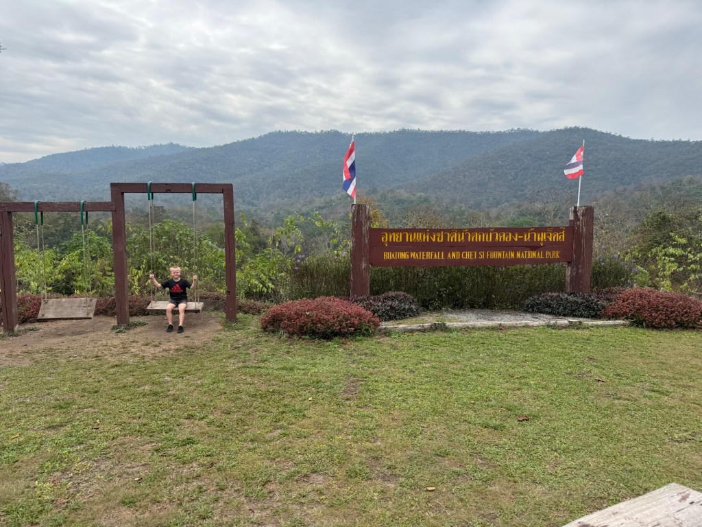 Sticky Waterfalls Chiang Mai entrance sign with mountain views and a child sitting on a swing at Bua Tong Waterfalls
