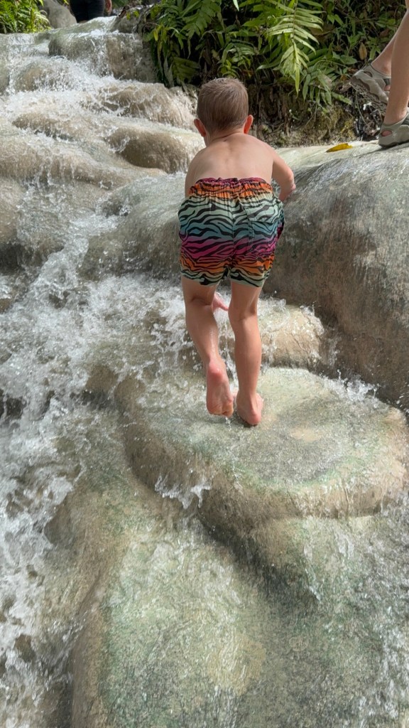 Child climbing the Sticky Waterfalls in Chiang Mai on the natural limestone surface with flowing water