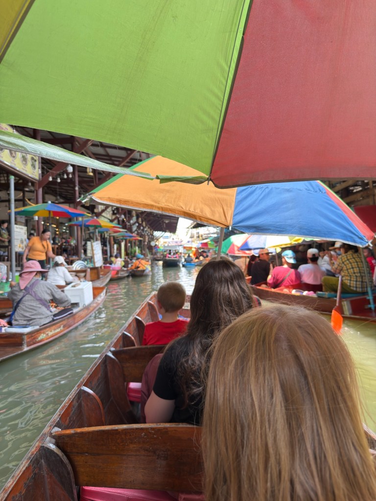 Boat ride through Damnoen Saduak Floating Market with vendors and colorful umbrellas lining the canal