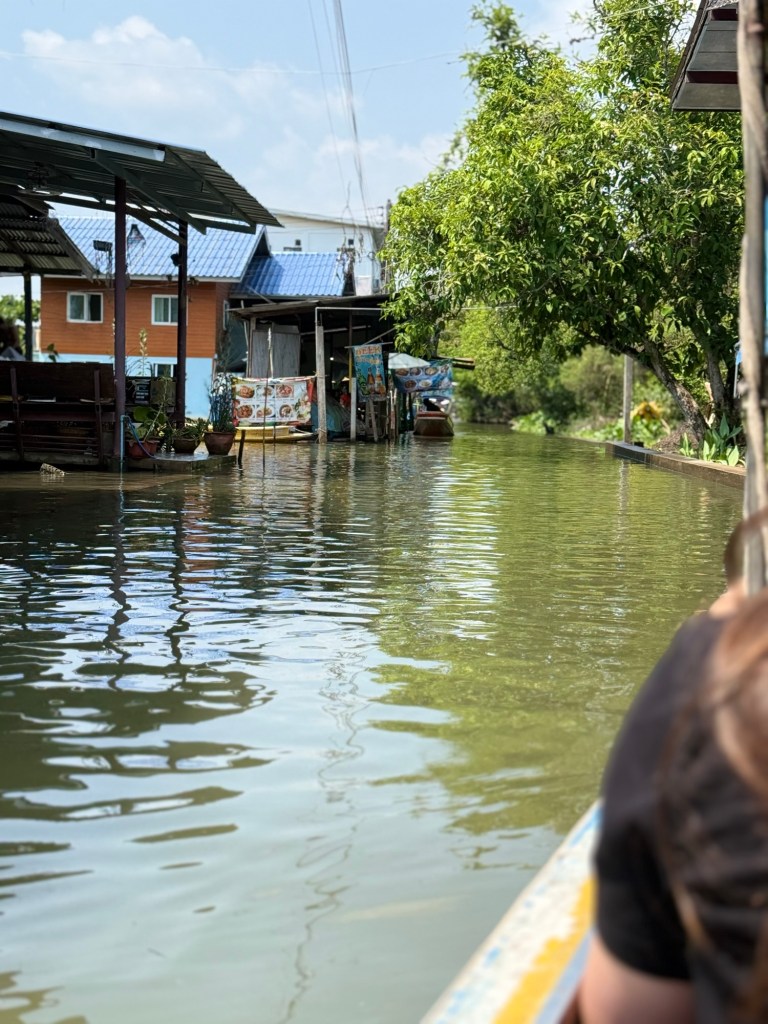Longtail boat ride through a quieter canal near Damnoen Saduak Floating Market with homes and greenery along the water