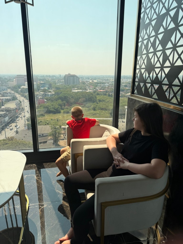 Children looking out over Chiang Mai city from a condo window during slow travel in northern Thailand