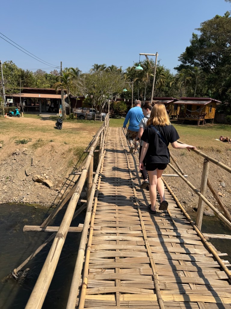 Family crossing a bamboo footbridge near Pai Walking Street in Pai, Thailand.