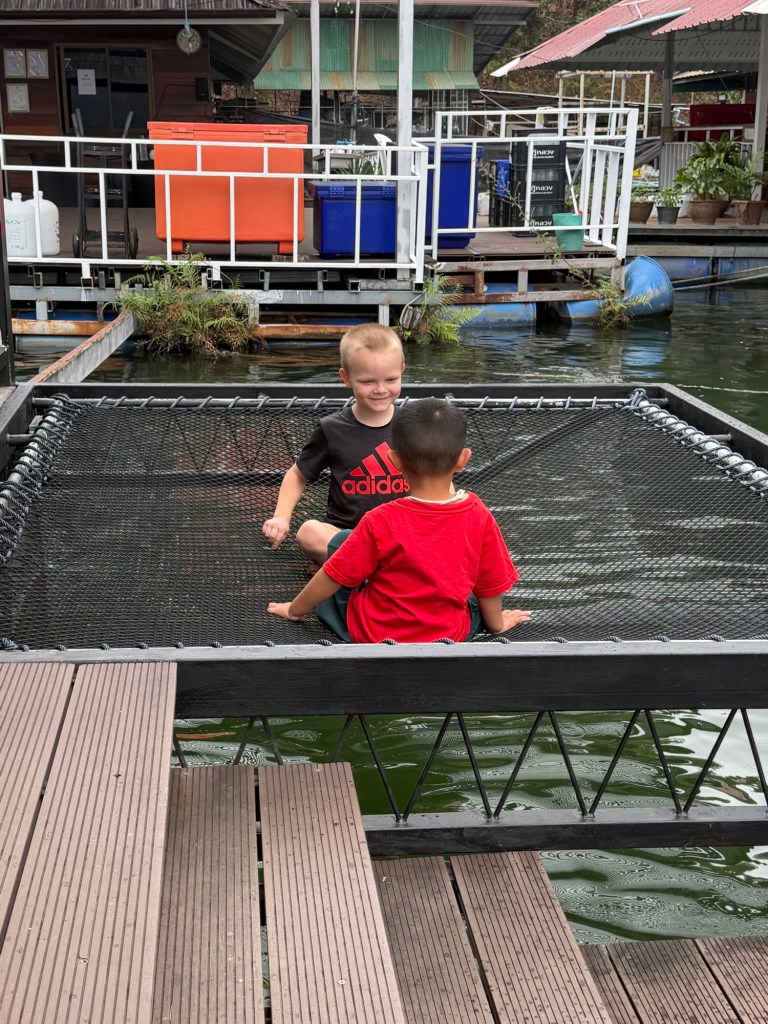 Two children sitting and playing together on a net platform over the water at a floating restaurant on Mae Ngat Dam in Sri Lanna National Park, Chiang Mai
