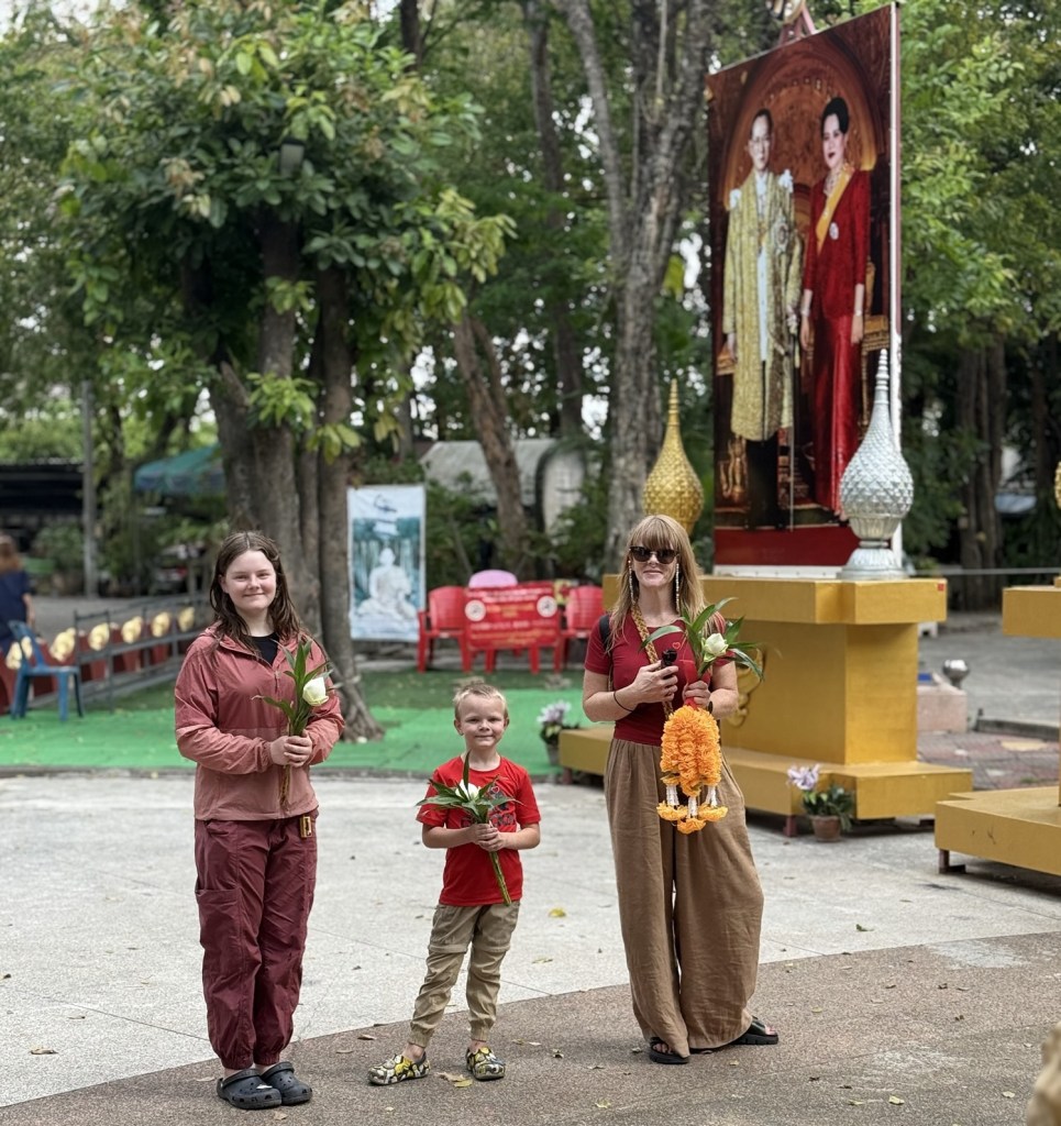 Family visiting temple in Thailand with kids holding flower offerings
