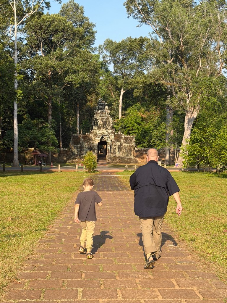 Father and young boy walking toward temple entrance at Angkor complex in Cambodia