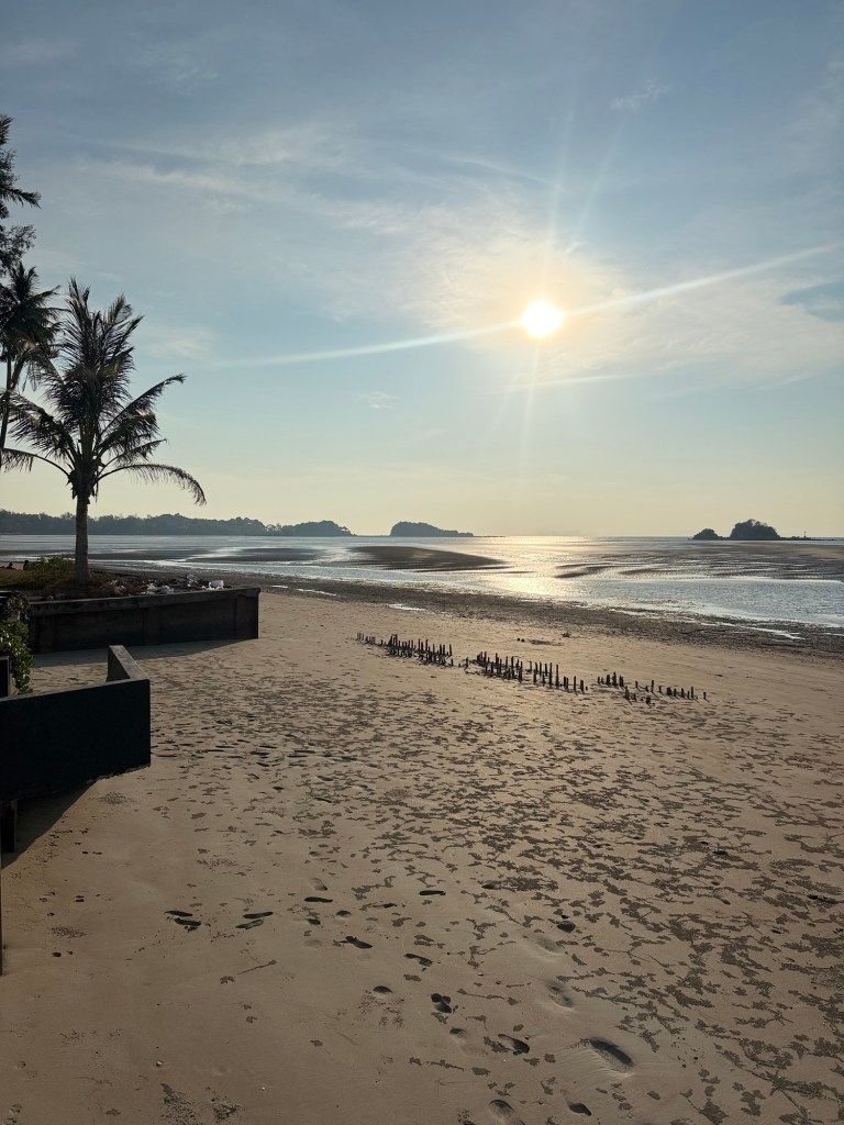 Morning view of the beach in Koh Lanta, Thailand with calm water, palm trees, and soft sunlight during low tide.